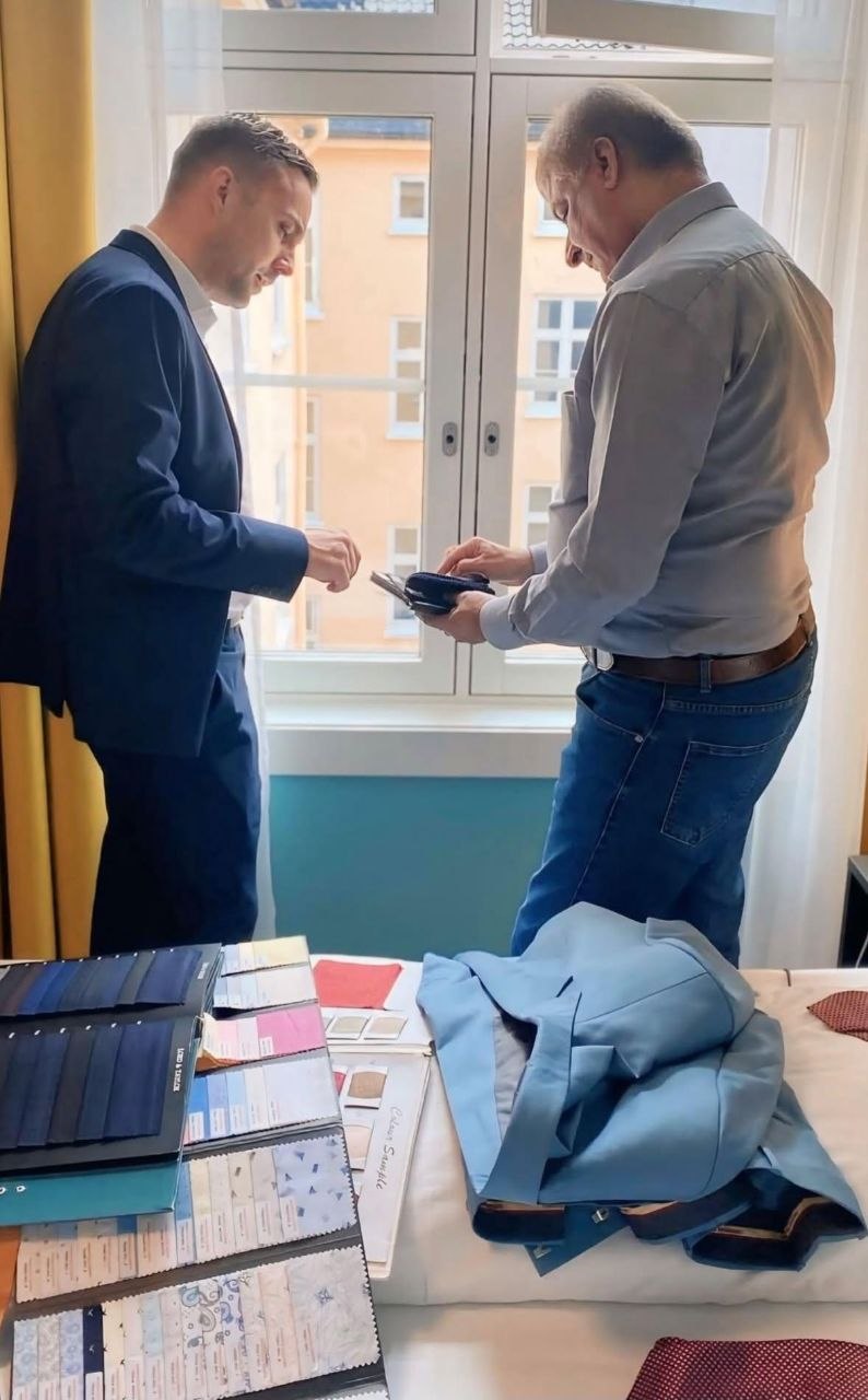 Real client photograph showing cloth books and a tailor discussing a navy jacket